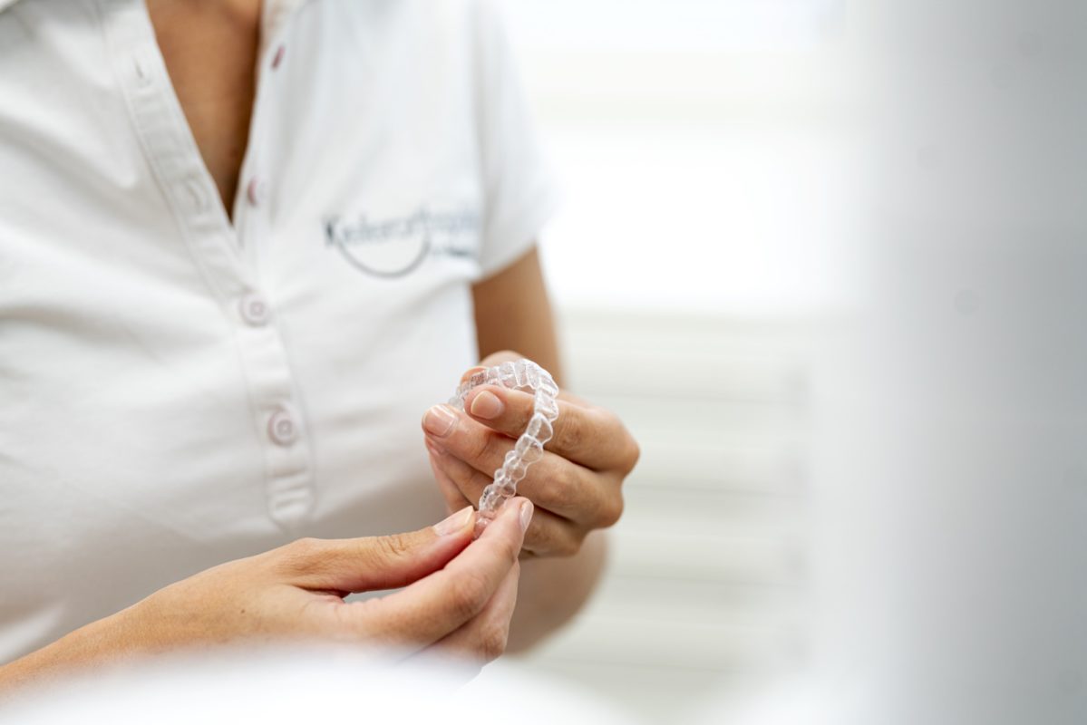Kieferorthopädin hält eine transparente Zahnspange (Aligner) in den Händen.