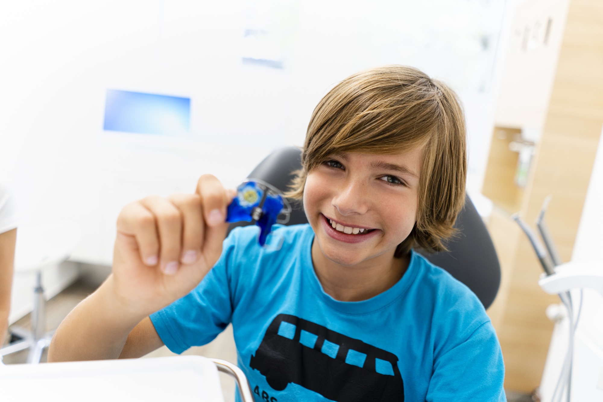 Junge in einer kieferorthopädischen Praxis zeigt stolz seine blaue Zahnspange.