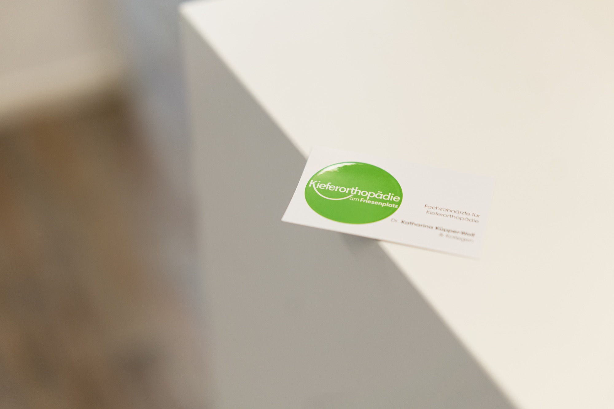 Visitenkarte der Praxis Kieferorthopädie am Friesenplatz auf einer weißen Theke.