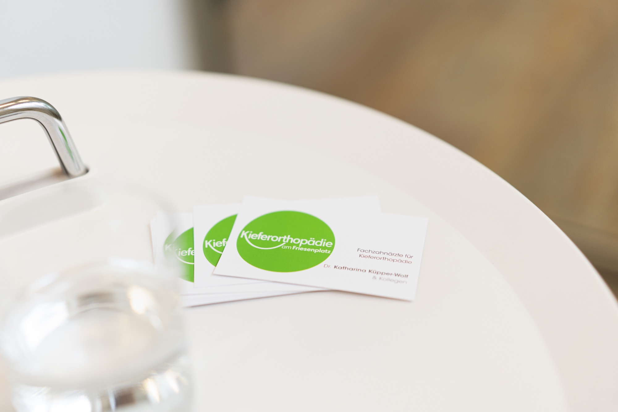 Visitenkarten der Kieferorthopädie am Friesenplatz liegen ordentlich auf einem weißen Tisch.
